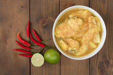 Yellow curry with snapper or sea bass and coconut shoot in white bowl on wooden table.Thai food and selective focus.