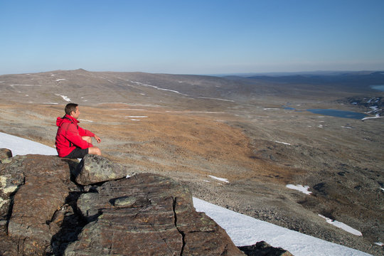 Hiker sitting on mountain, on the horizon the Halti Peak, view from southwest, summer 