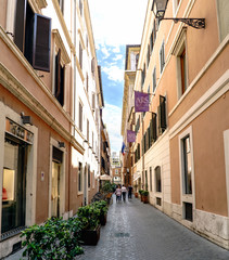Typical narrow cobbled shopping street of Rome, Italy. With people walking and a blue sky with clouds