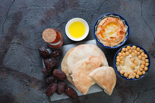 Homemade hummus with pita bread and date fruits on a dark textured background, view from above, horizontal shot