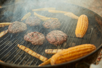 Beef patties and fresh corncobs on a BBQ