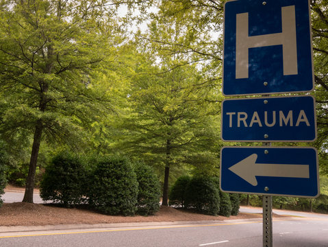 Hospital trauma center traffic sign with left arrow on peaceful tree-lined street