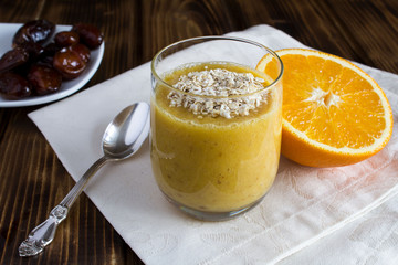 Healthy breakfast: smoothie from orange, dates and oat flakes on the wooden background