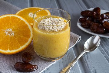 Breakfast with smoothie from orange, dates and oat flakes on the grey wooden background