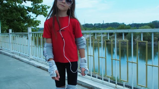 The child rolls on rollers. A little girl in sunglasses and headphones goes rollerblading.