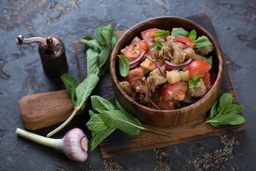 Salad with baked eggplants, fresh tomatoes and mint served in a wooden bowl on a rustic chopping board, studio shot
