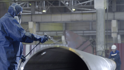 Male holding spray gun and painted steel. Man paints pipe atomizer