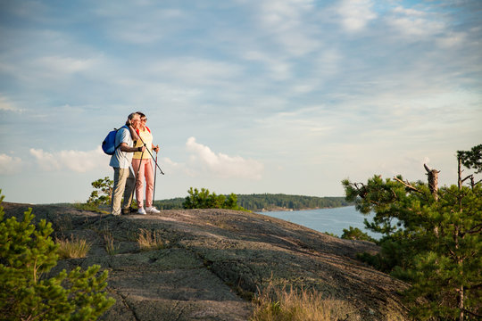 Active senior couple hiking on the top of rock, exploring. Mature man and woman Happily smiling. Nordic walking, trekking. Scenic view of gulf and sea. Healthy lifestyle. Finland.