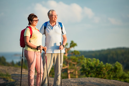 Active senior couple hiking on the top of rock, exploring. Mature man and woman Happily smiling. Nordic walking, trekking. Scenic view of gulf and sea. Healthy lifestyle. Finland.