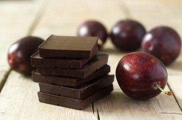A stack of chocolate slices and plums on a wooden table. Rustic style, selective focus.