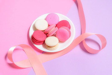 Homemade Colorful macaroons or macaron on White plate with copyspace on pink and purple background