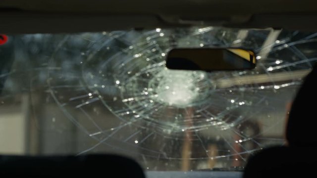  View from interior of car, windshield being smashed with a baseball bat.