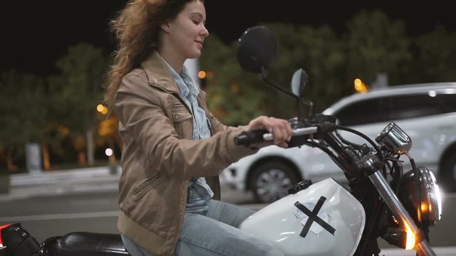 Beautiful young woman riding an old cafe racer motorcycle on street. Female biker at night sity. Slow motion 
