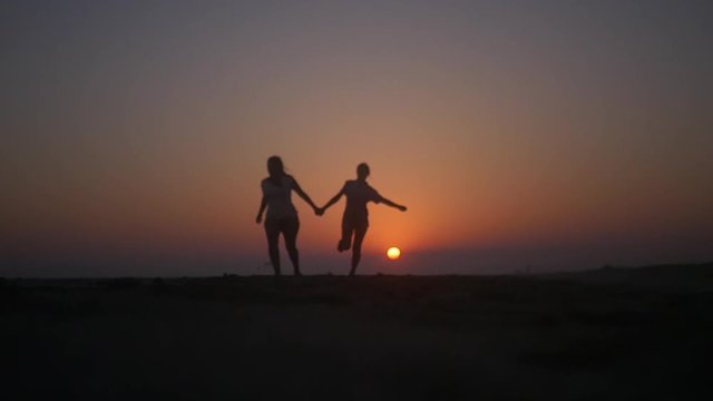 Two friends hold hands and jump on the beach at sunset. HD, 1920x1080. slow motion.