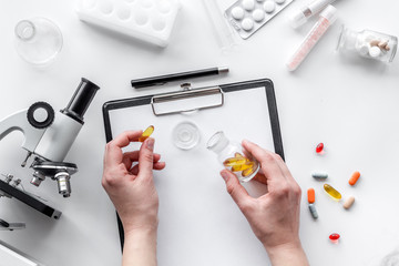 Obraz premium Do medcal tests. Hands hold pills near microscope on white background top view