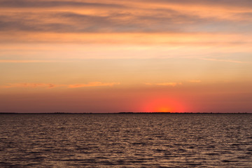 Fototapeta premium Beautiful scarlet sunset and calm waves on the lake