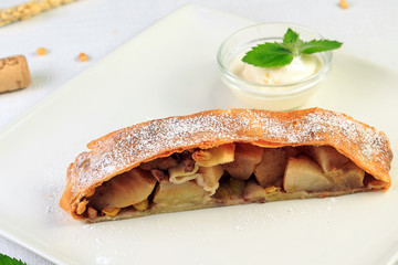 Traditional piece of apple strudel with powdered sugar and mint closeup on a table. horizontal