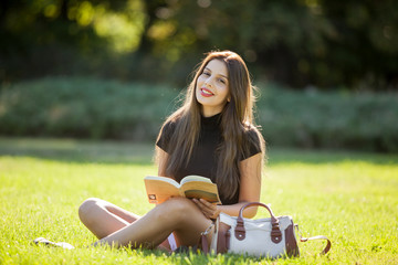 Portait of Beautiful young woman enjoying reading outside in the park on sunny day