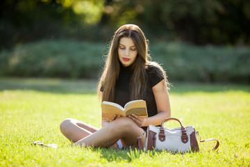 Portait of Beautiful young woman enjoying reading outside in the park on sunny day