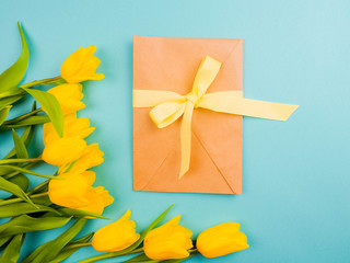 Love, romance, greetings, celebration concept - yellow tulips on blue background. delicate petals from a Tulip with a gift envelope at the center