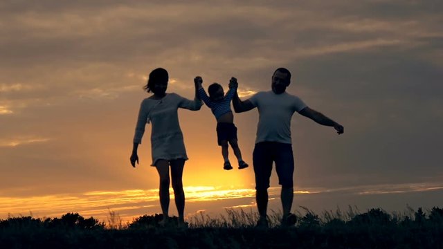 Happy family running in the field at sunset. Silhouette of a family on a summer evening. The concept of love of family happiness