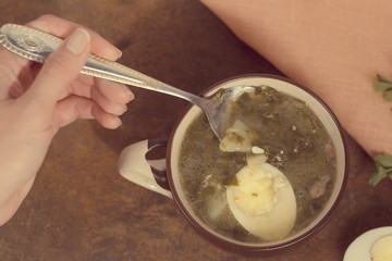 Woman eats a spoon with oxalic soup.