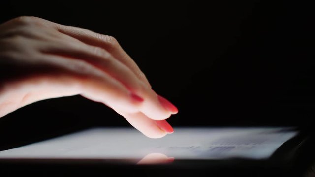 Internet browsing on the tablet. Female fingers scroll text screen, close-up. Side view