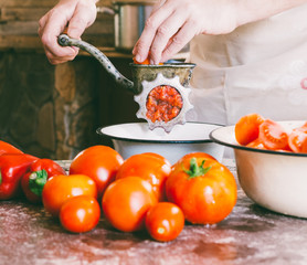 male chef grinds pieces of ripe tomatoes in an old vintage manual grinder to make homemade sauce, ketchup
