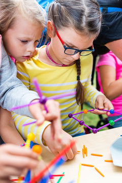 Two Little Girls Playing With Lots Of Colorful Plastic Sticks Kit Indoors. Kids Having Fun With Building  Geometric Figures And Learning Mathematics In Preschool Or Primary Class Of School