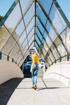 young woman model walking in alley way bridge with chain link fence