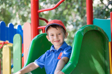 Fototapeta na wymiar Little boy smiling on a playground outdoors in summer. Having fun on a slide.