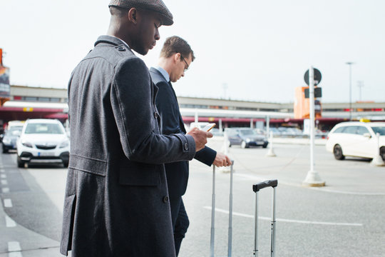 Two Business Travelers Using Smartphones as They Wait For Taxi