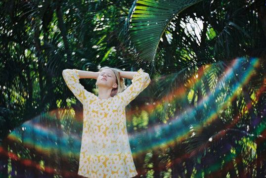 girl in yellow floral dress with rainbow flare against green palms