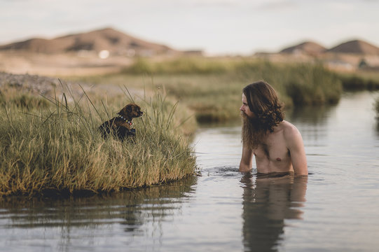 A handsome bearded man with his dogs in beautiful desert hot springs during the golden hour