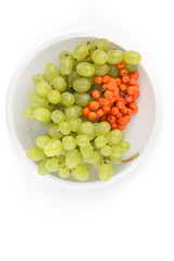 Green grapes and orange ashberry on a white background on a plate in minimalism style