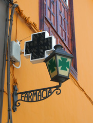 old spanish pharmacy sign in wrought iron on a yellow wall with green cross farmacia = pharmacy