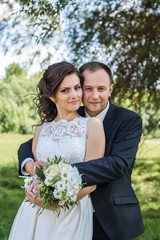 couple in wedding attire with a bouquet of flowers and greenery is in the hands against the backdrop of trees, the bride and groom