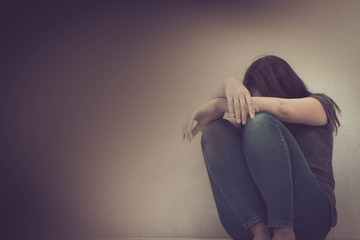 sadness young woman sitting on wood floor looking at empty dark area feeling unhappy and afraid on white wall background with battered abused woman concept.