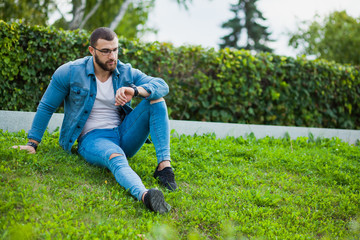 Naklejka na ściany i meble Young muscular man in casual wear sit on grass look at wrist watch