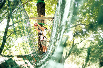 Happy little boy passing the cable route high among trees, climbing and playing, extreme sport in adventure park