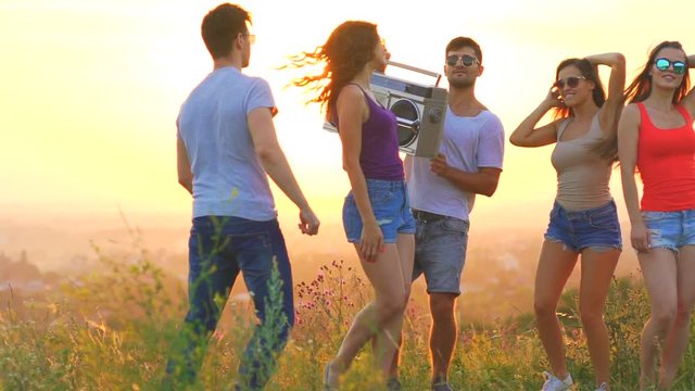 The young people with a boom box dancing on a sunset background. slow motion