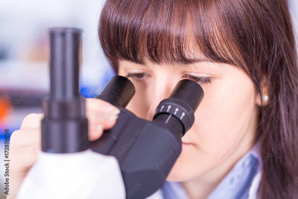 Wall mural Doctor woman working  a microscope. Female scientist looking through a microscope in lab. Student girl looking in a microscope, science laboratory concept