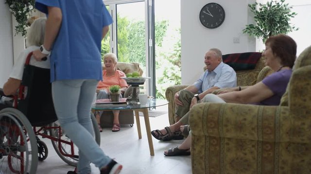 Caring staff in retirement home taking care of elderly residents and serving tea and cookies.