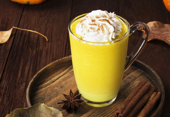 Pumpkin latte with spices (cinnamon, anise) and whipped cream on a wooden background. Copy space. Food background