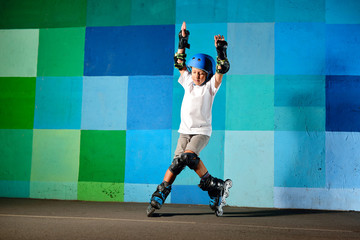Cute little boy on roller skates running against the blue graffiti wall - obrazy, fototapety, plakaty
