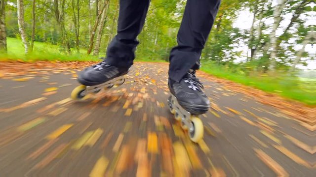 Outdoor inline skating on wet slippery asphalt in autumnal forest. Man legs in black running trousers. Quick movement of inline boots on road covered with autumnal ccolorful leaves.. 