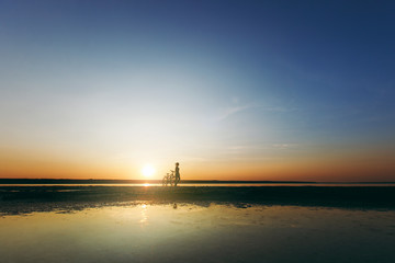 Silhouette of a sporty girl in a suit standing near a bicycle in the water at sunset on a warm summer day. Fitness concept. Sky background