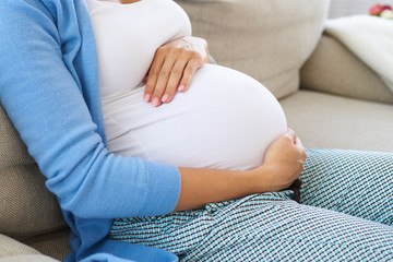 Future mother sitting on sofa relaxing, touching tender her belly