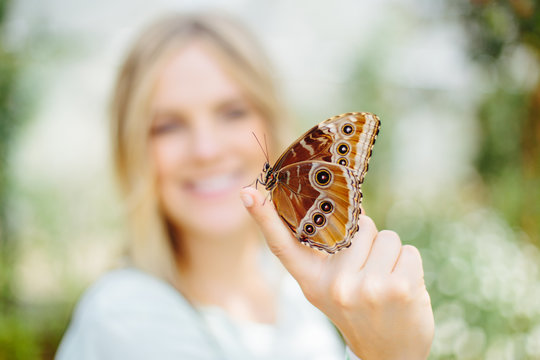 Young Blonde Woman Holding Orange Butterfly On Tip Of Finger