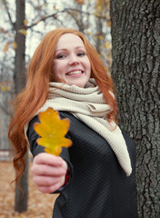 young woman stand near tree in autumn park and give yellow leaf